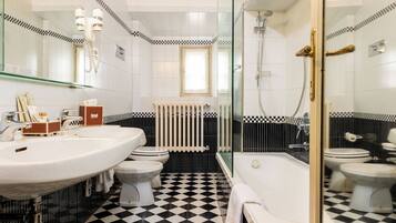 Un baño con un lavamanos grande de color blanco, dos inodoros, una bañera y una zona de ducha con mampara de vidrio.