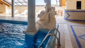 A pool area with a statue, lounge chairs, and a tiled floor.