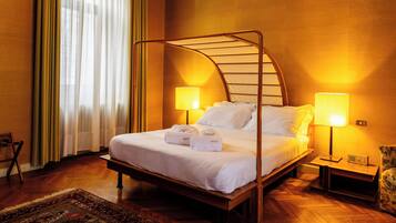 Un letto rifatto con lenzuola e asciugamani bianchi, una testiera in legno, due abat-jour e un comodino in legno con una radio.