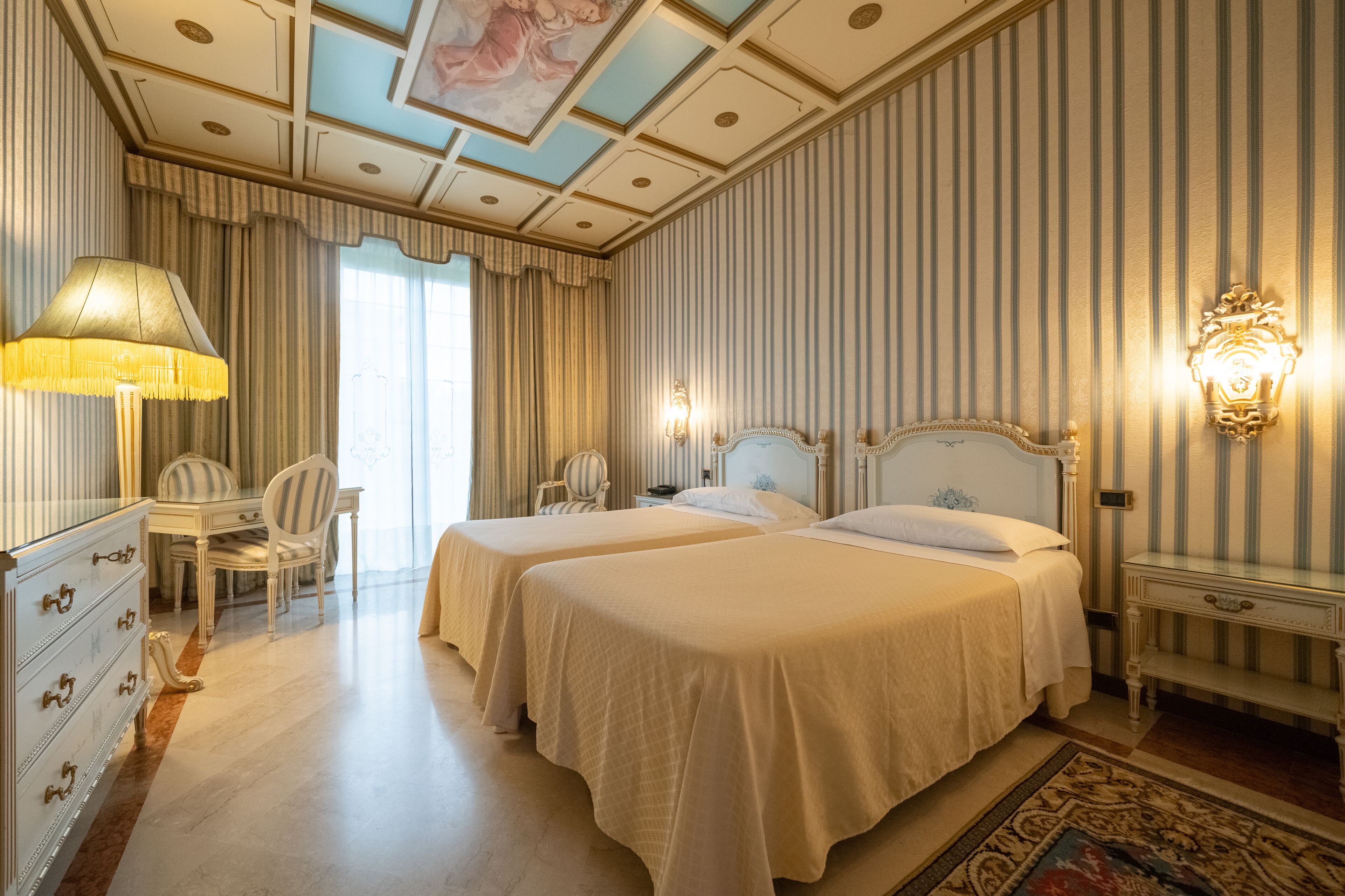 Una camera d'albergo con due letti, una scrivania, una sedia e un comò.