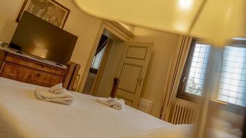 A hotel room with a bed, a flat-screen TV on a wooden dresser, and a window with blinds.