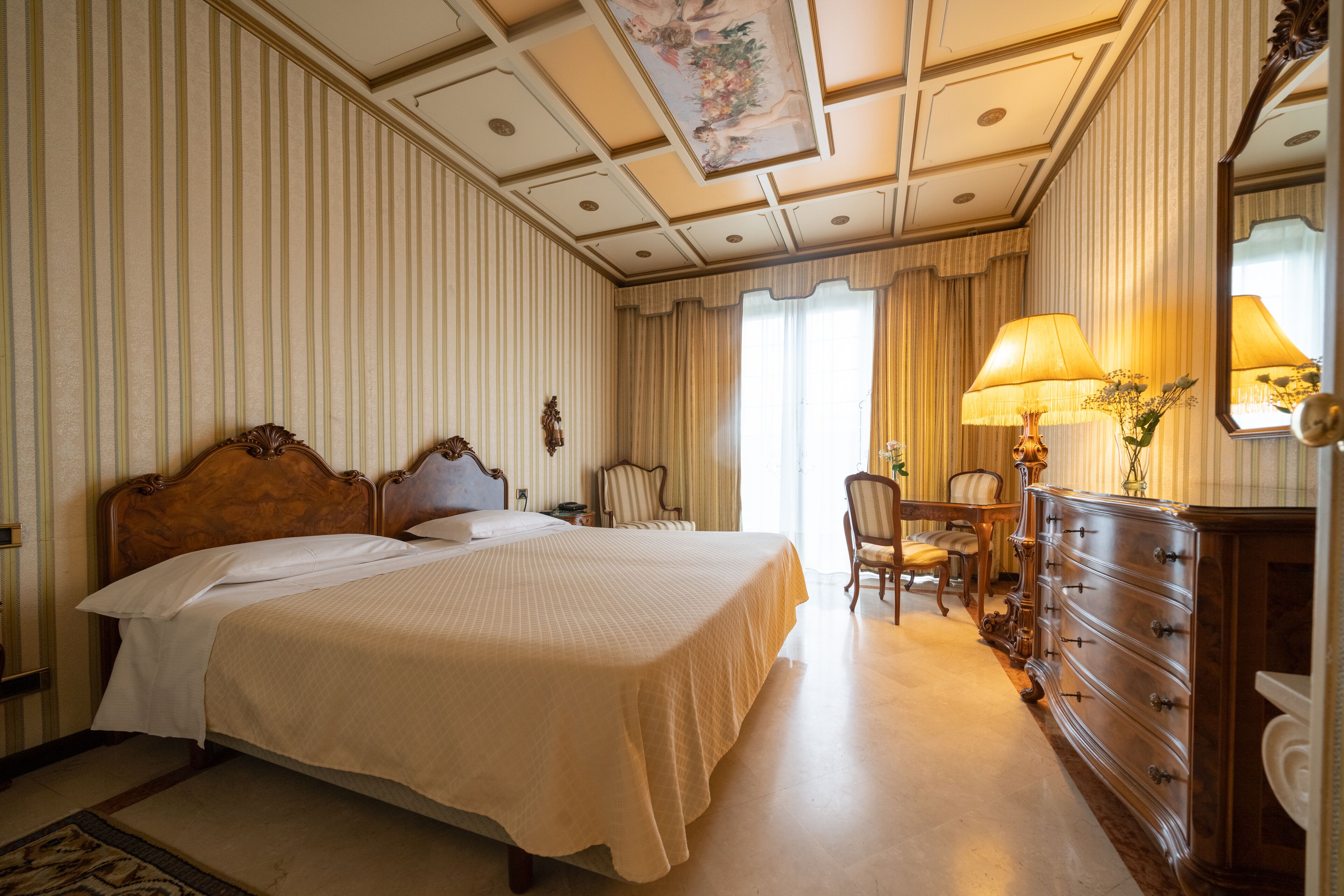 A hotel room with a large bed, a desk with a chair, a dresser, and a mirror.