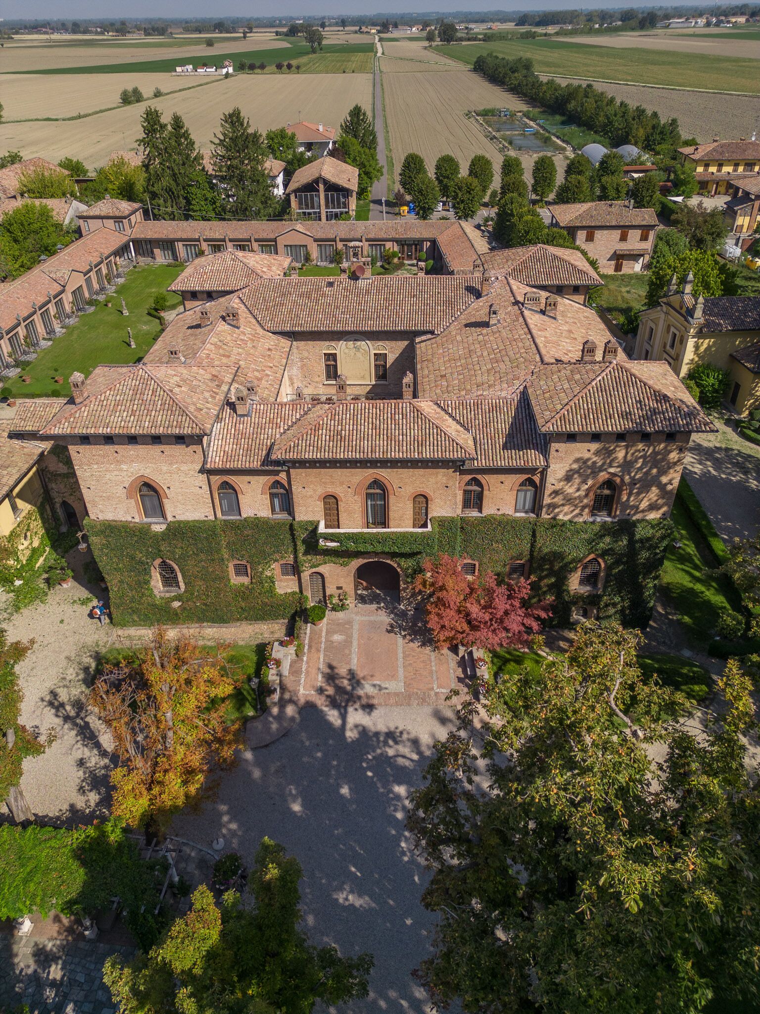 Un edificio grande e histórico con un patio, rodeado de árboles y campos.