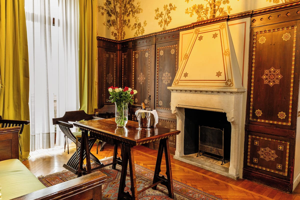 Ein traditionell eingerichtetes Zimmer mit einem Holztisch, Stühlen, einer Vase mit Blumen und einem Kamin.