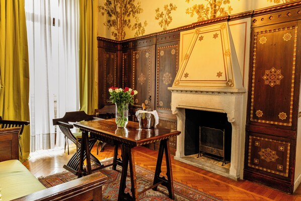 Una habitación tradicional con una mesa de madera, sillas, un florero con flores y una chimenea.