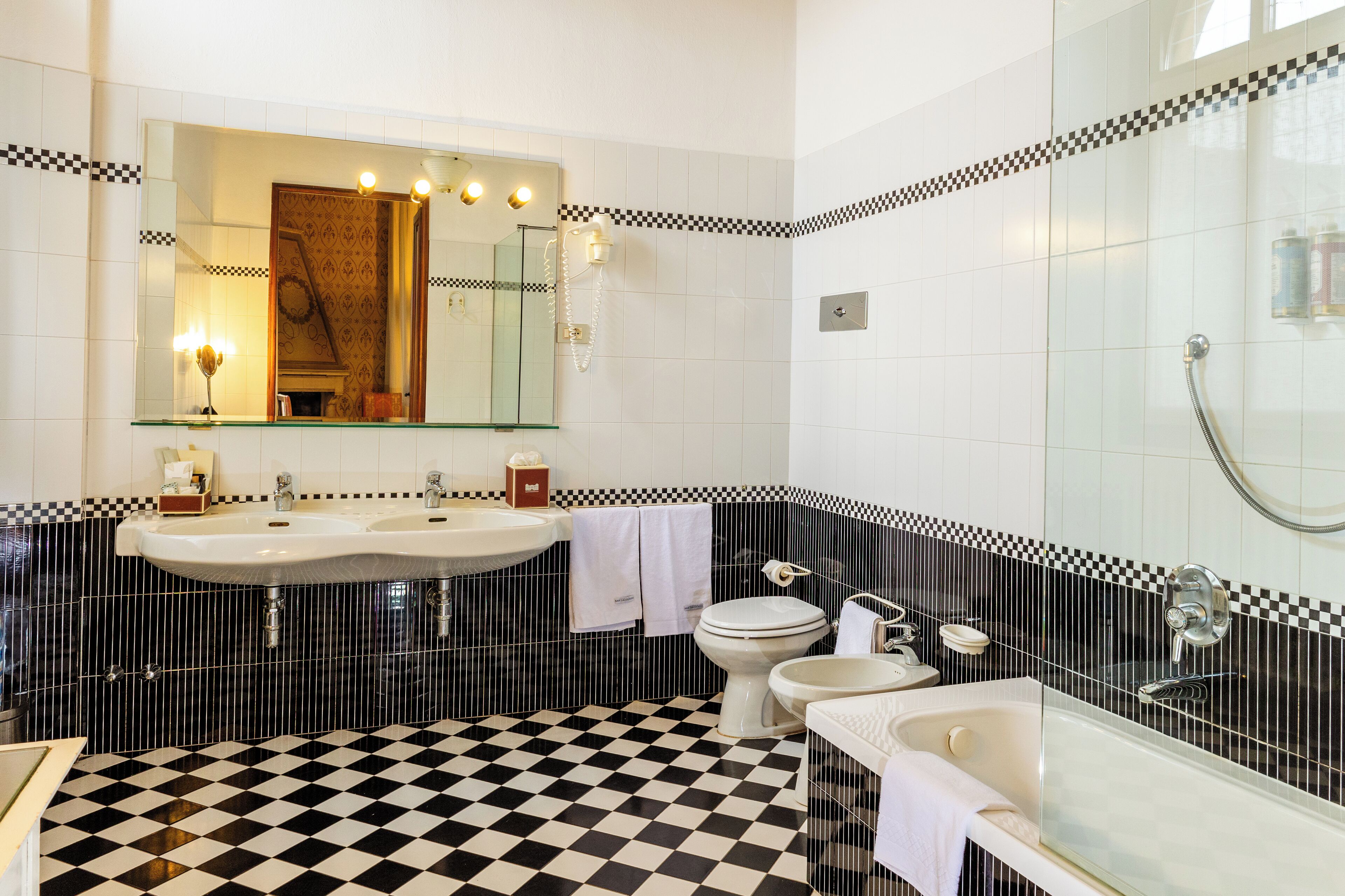 A bathroom with a checkered floor, two sinks, a toilet, and a bathtub.