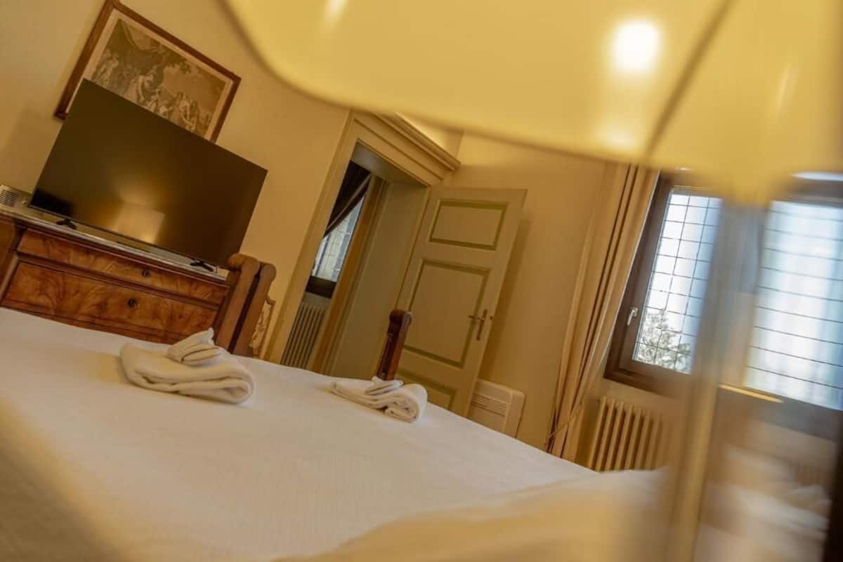 Ein Hotelzimmer mit einem Bett, einem Fernseher auf einer Holzkommode, einer Tür und einem Fenster mit Jalousien.