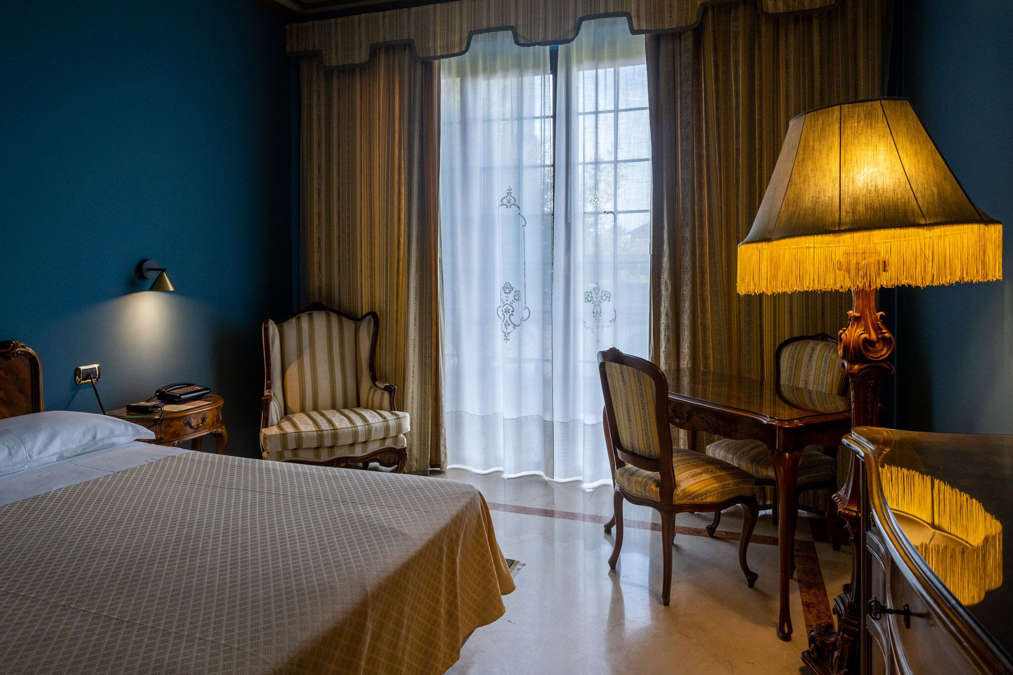 Una habitación de hotel con una cama grande, dos sillones, un escritorio con lámpara y una ventana con cortinas.