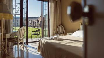 Une chambre d’hôtel avec un lit, un bureau, une chaise et une vue sur une cour intérieure, accessible par une porte vitrée.