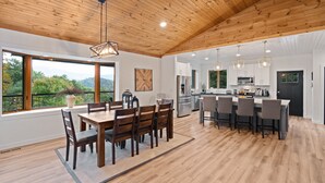 Una cocina amplia con electrodomésticos modernos, un comedor con mesa y sillas de madera, y ventanas grandes que ofrecen vistas al exterior.