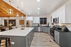 A modern kitchen with a large island, stainless steel appliances, and a wooden ceiling.