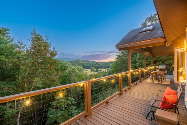 A wooden deck with a railing, outdoor furniture, and a view of a forested landscape.
