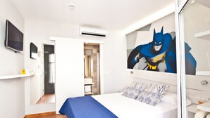 Quarto de hotel com cama, TV, ar condicionado e um mural do Batman na parede.