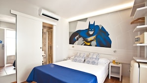A bedroom with a bed, a wall-mounted air conditioner, a small bedside table, and a wall painting of a superhero. - Ryans Pocket (Ibiza Town)