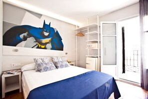 A hotel room with a large Batman poster, a neatly made bed with blue bedding, a small bedside table with a magazine, and a wardrobe with a mirror. - Ryans Pocket (Ibiza Town)
