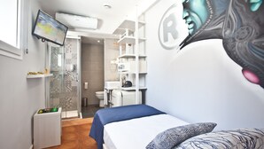 Quarto de hotel pequeno com cama, televisão, chuveiro e banheiro.