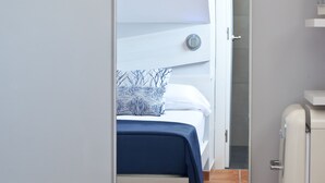 Um quarto com cama, espelho, um pequeno armário branco e piso de azulejos.