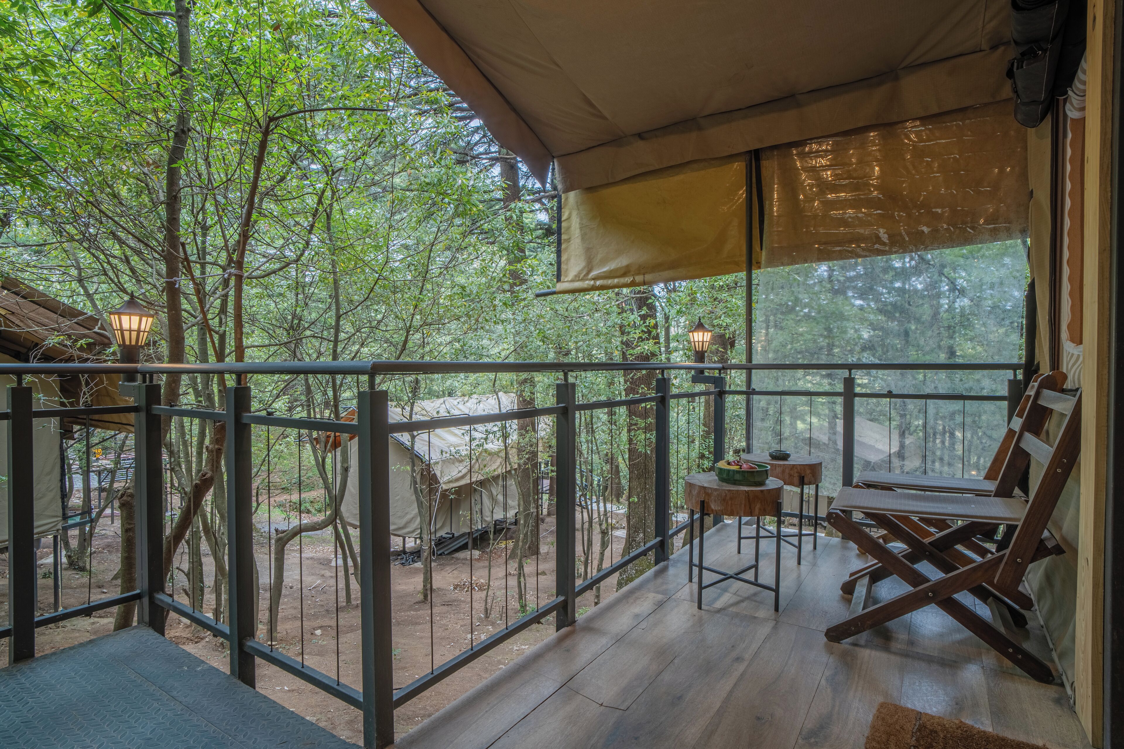 A wooden deck with a metal railing, a covered seating area, and a view of the surrounding forest.