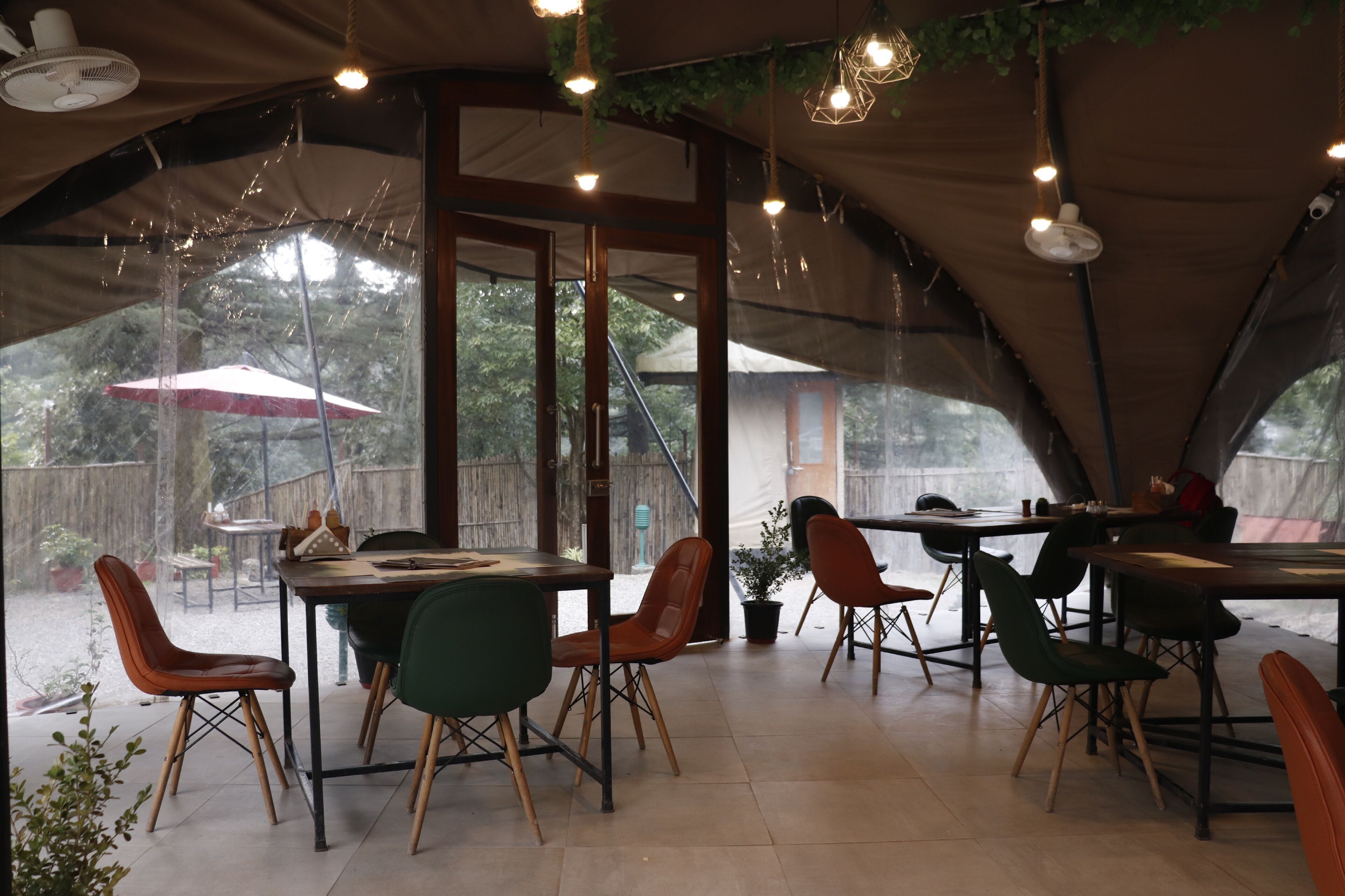 A tented dining area with tables and chairs, large windows, and hanging lights.
