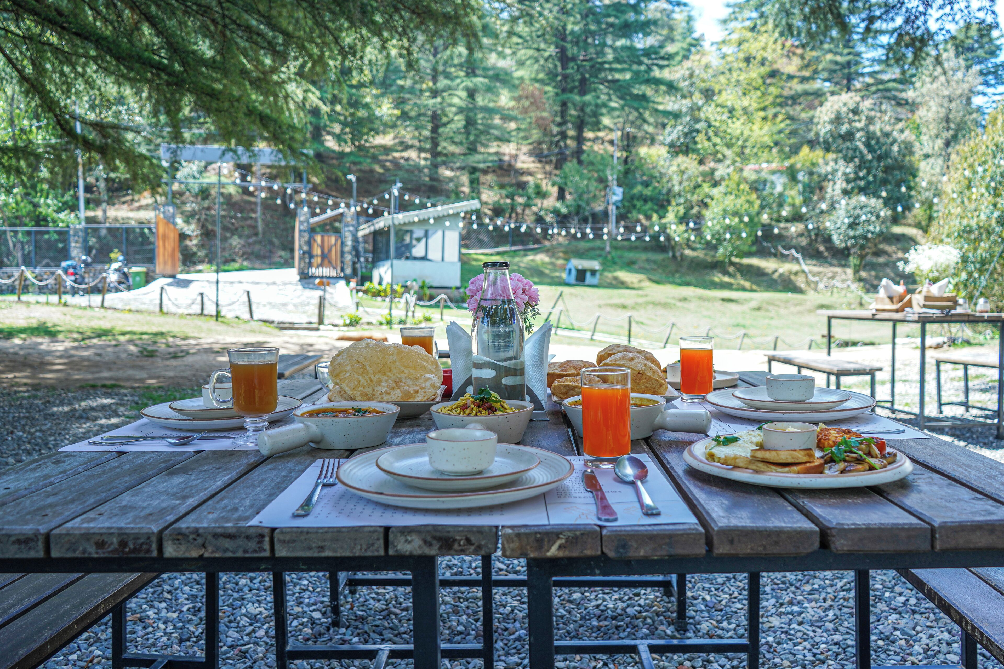 Una mesa de picnic dispuesta con varios platos, incluyendo un tazón de sopa, una porción de papas fritas y un vaso de jugo de naranja.
