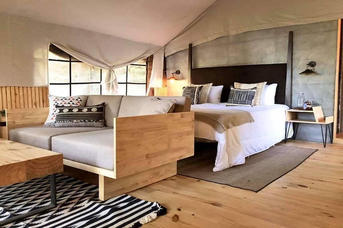 A cozy bedroom with a bed, a sofa, a wooden nightstand, and a window with curtains.