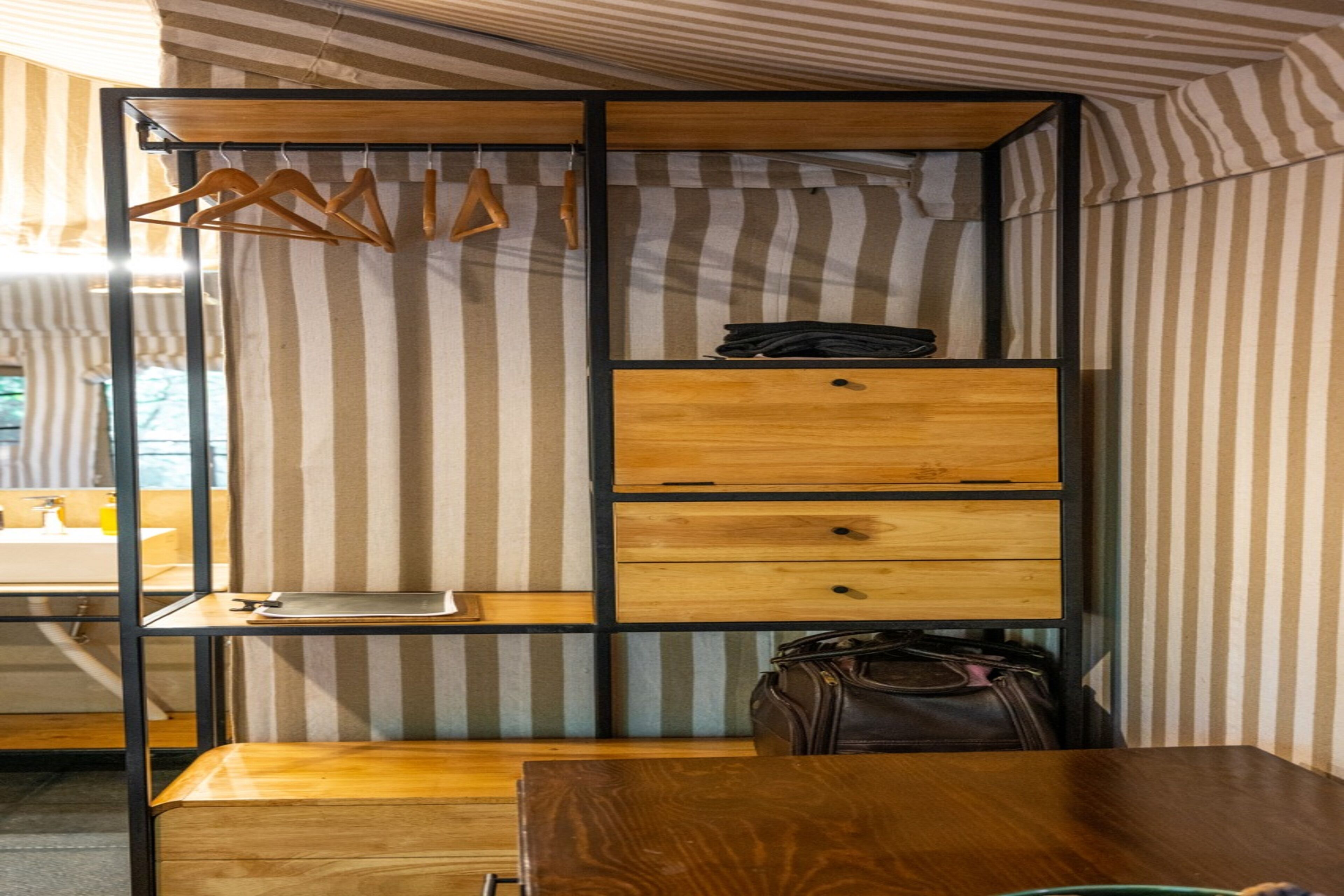 Una habitación compacta con pared a rayas, un escritorio de madera, un perchero y un pequeño armario de madera.