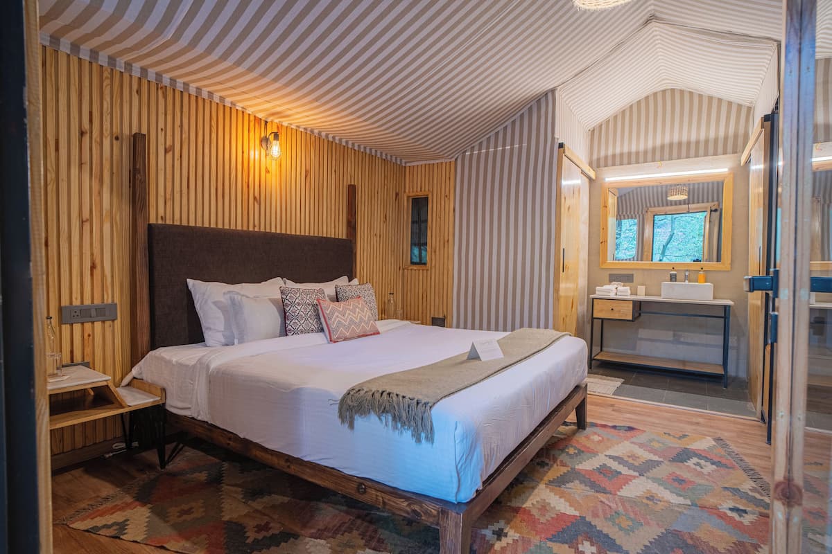 A wooden-paneled room with a large bed, a bedside table, a mirror, and a small window.