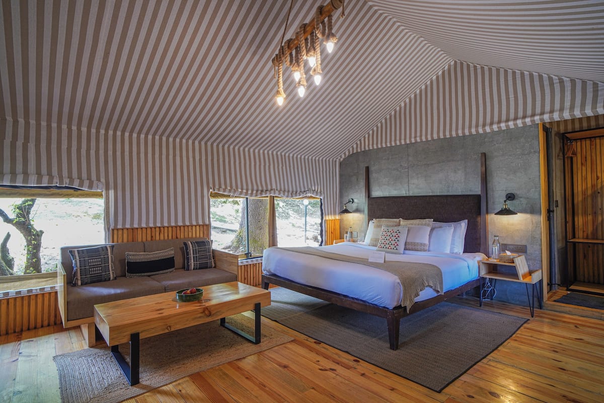 A bedroom with a large bed, a sofa, a wooden coffee table, and a nightstand with a lamp.