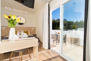 Ein modernes Hotelzimmer mit einem Bett, einem Schreibtisch mit Blumen, einem runden Spiegel und einem Balkon mit Tisch und Stühlen.