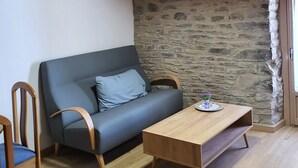 Una habitación acogedora con techo de madera, pared de piedra, un sofá gris, mesa de centro de madera y una silla.
