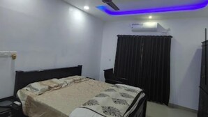 A bedroom with a bed, a ceiling fan, a nightstand, a dresser, and a window with curtains. - Rain Homestay (Ambalapuzha)
