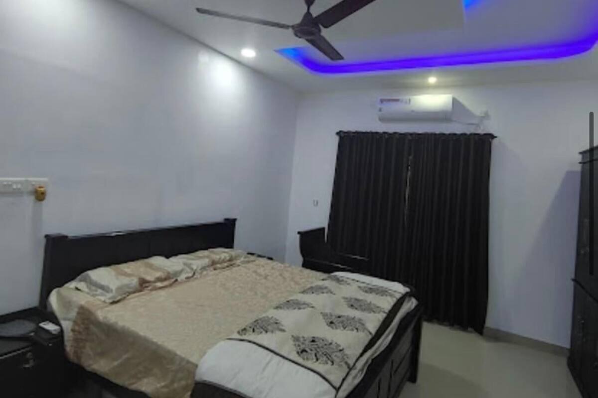 A bedroom with a bed, a ceiling fan, a nightstand, a dresser, and a window with curtains.