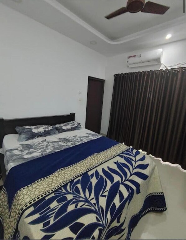 Quarto com cama, ventoinha no teto, ar condicionado e janela com cortinas.