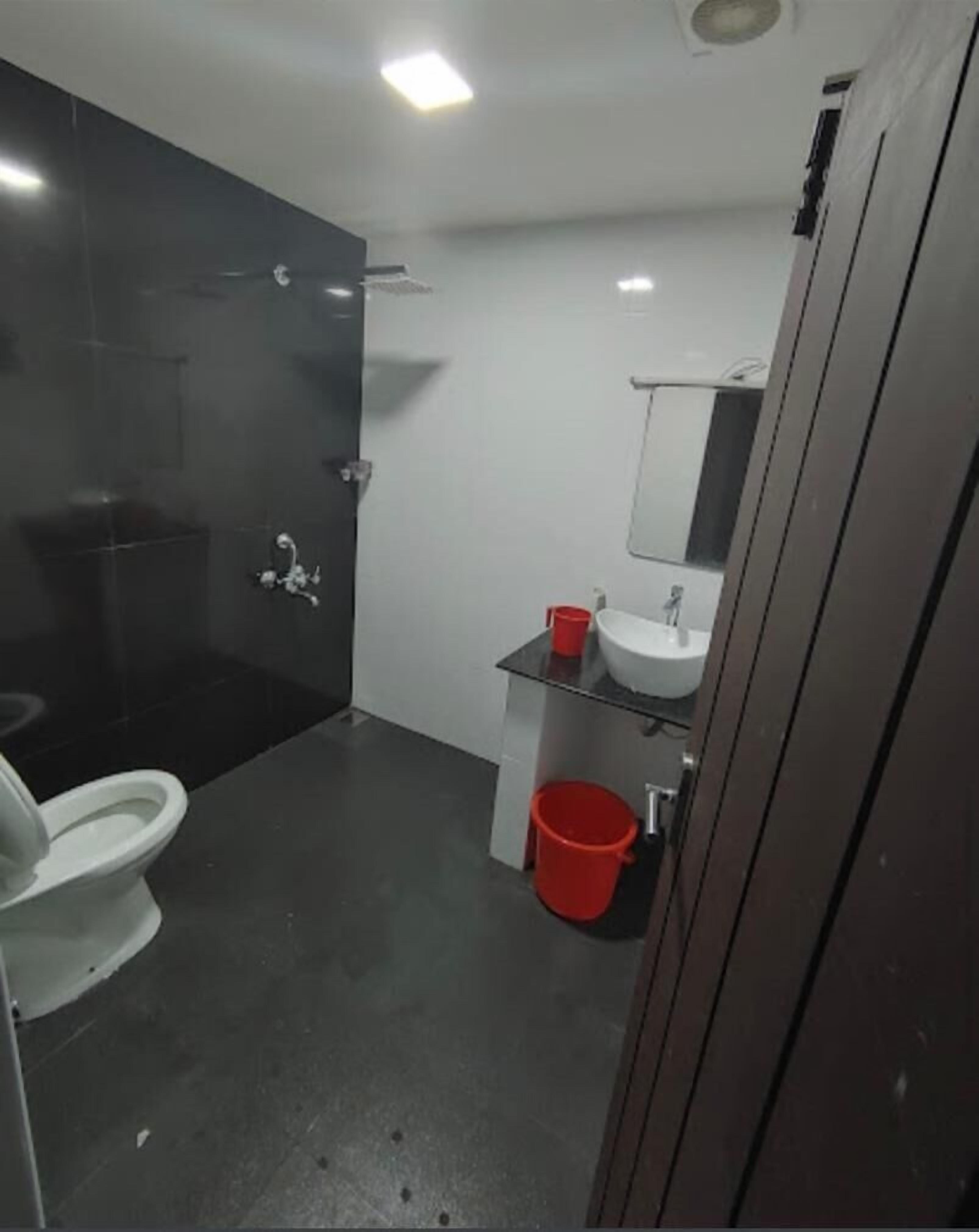 Un baño con inodoro, lavamanos, espejo y un cubo rojo.