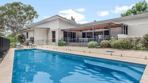 Una casa moderna con piscina, patio techado y zona de estar al aire libre.
