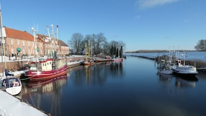 Ein Hafen mit mehreren angedockten Booten, ein Gebäude mit rotem Dach und eine ruhige Wasserfläche, die die Umgebung spiegelt.