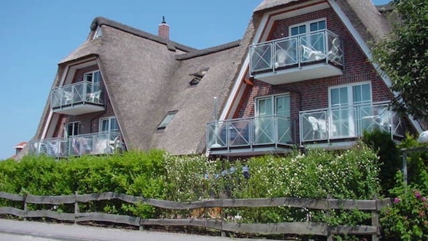 Ein zweistöckiges Haus mit Strohdach, einem Balkon und einem Holzzaun davor.