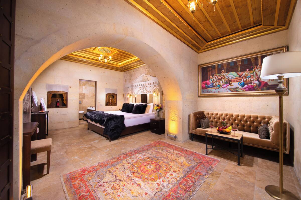 A spacious bedroom with a large bed, a sofa, a coffee table, and a painting on the wall.