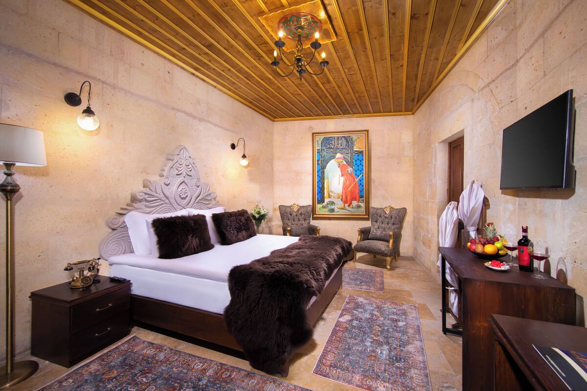 A bedroom with a large bed, a desk with a flat-screen TV, a chair, and a painting on the wall.