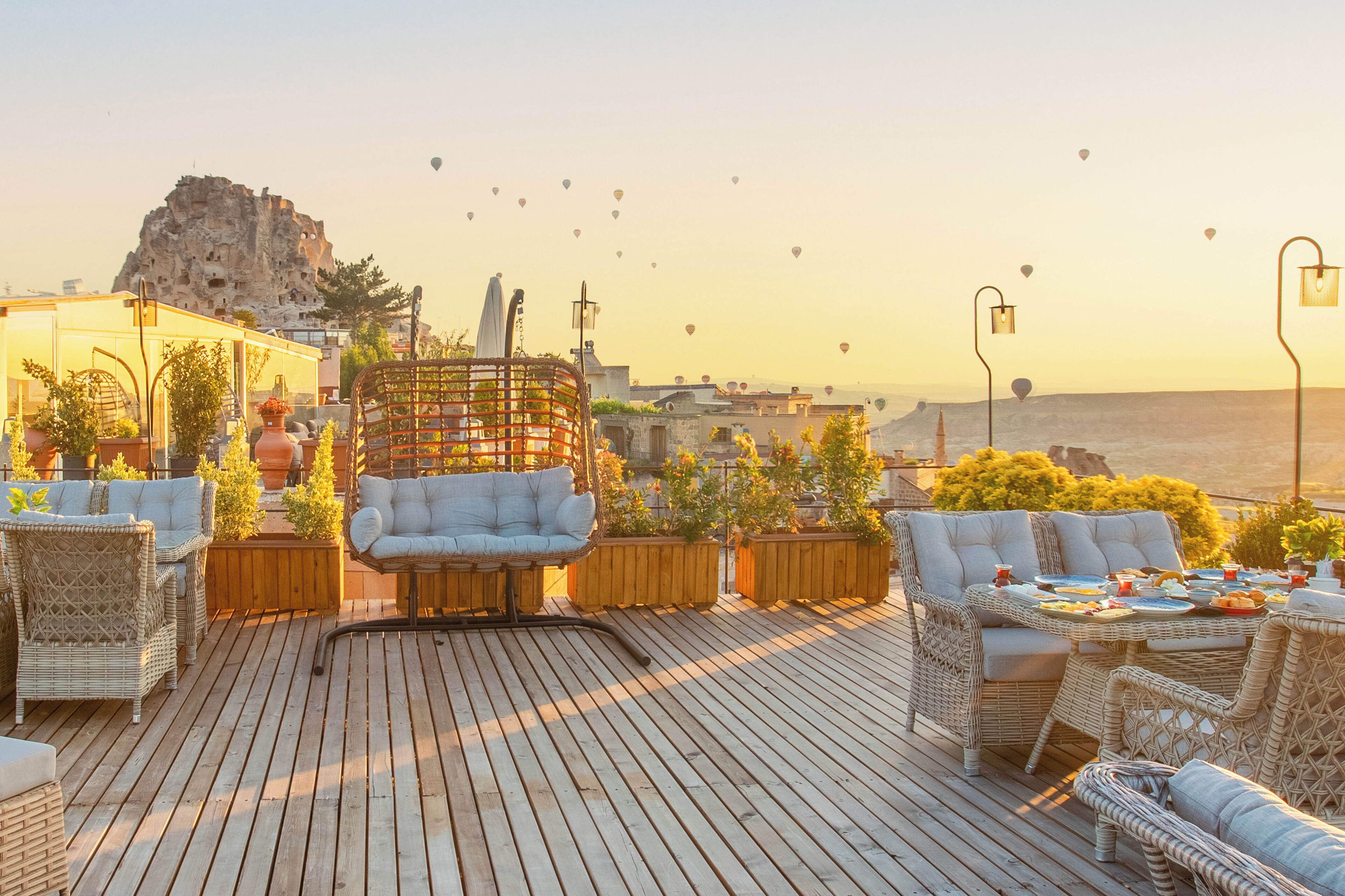Una terrazza sul tetto con mobili in vimini, piante in vaso e vista su una montagna rocciosa e sullo skyline della città.
