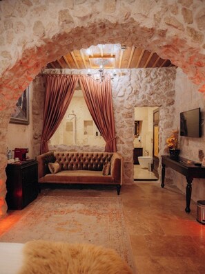 Una habitación con un arco de piedra, un sofá con textura, suelo de madera y pared de piedra.