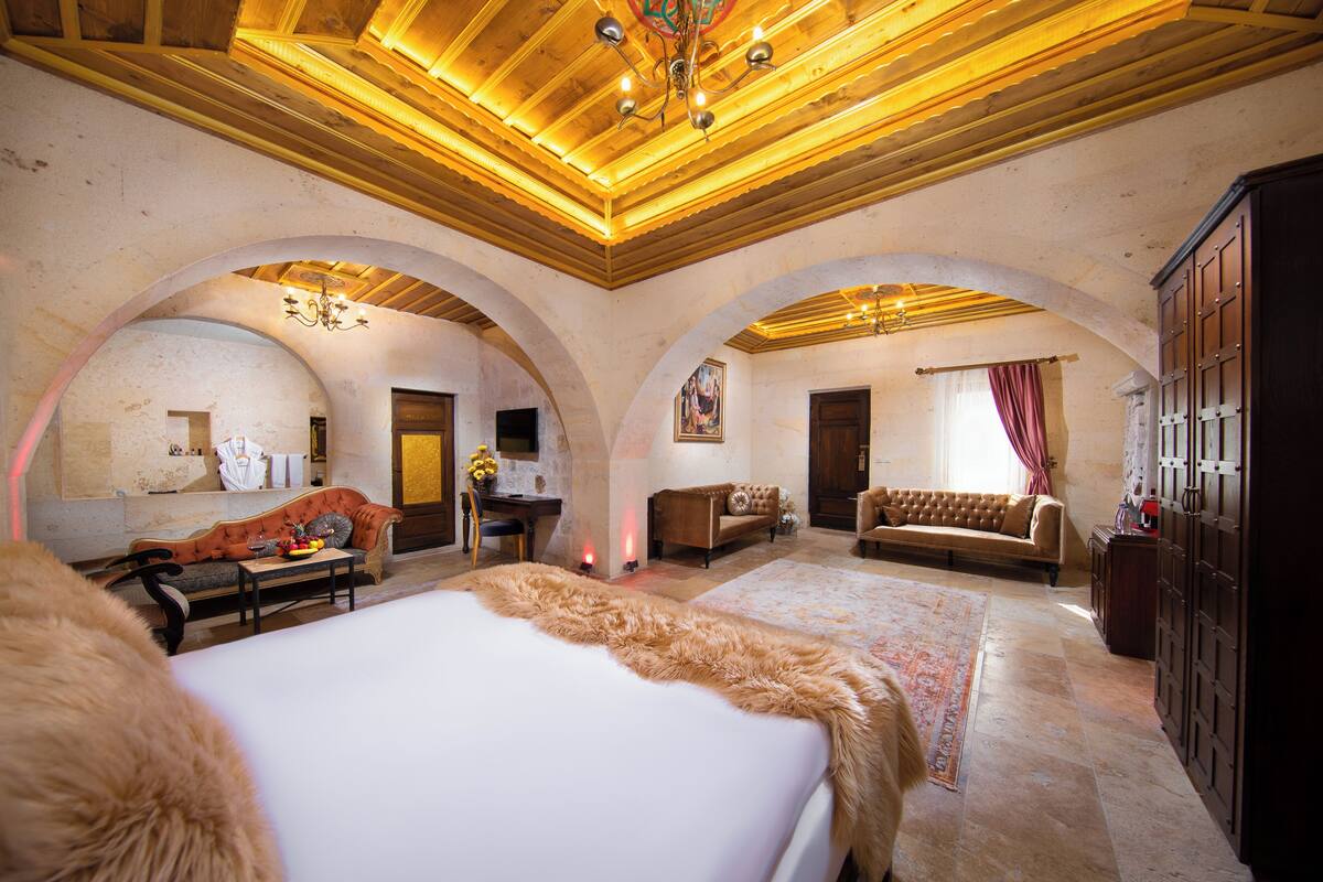 A spacious room with a large bed, a sofa, and a desk. There are arched ceilings and a chandelier.