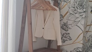 A room with a wooden coat rack holding a beige coat, a woven basket, and a patterned rug on the floor. - Les Arcades Studio in the heart of town, near Puy du Fou, with Wi-fi, Netflix, Canal+. (Cholet)
