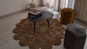 A living room with a flat-screen TV mounted on the wall, a small table with a remote control, and a decorative vase with pampas grass. - Les Arcades Studio in the heart of town, near Puy du Fou, with Wi-fi, Netflix, Canal+. (Cholet)