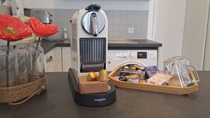 A kitchen counter with a coffee maker, two glass jars with red flowers, and a tray with coffee pods and a glass carafe. - Les Arcades Studio in the heart of town, near Puy du Fou, with Wi-fi, Netflix, Canal+. (Cholet)