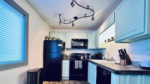 Une cuisine avec un sol carrelé, un réfrigérateur noir, un four à micro-ondes, une cuisinière et un lave-vaisselle.