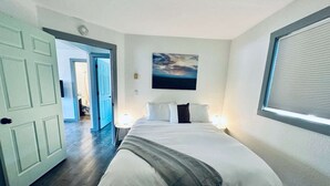 Une chambre à coucher avec un lit, un tableau, une fenêtre avec des stores et une porte donnant sur une autre pièce.