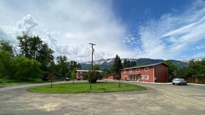 Un bâtiment à la façade rouge, un parking et une montagne en arrière-plan.
