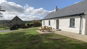 A white building with a stone wall and a wooden picnic table in front. - The Hidden Cottage, Ardara, Donegal. (Ardara)