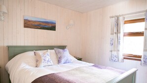 A bed with white and purple bedding, a green headboard, and a landscape painting on the wall. - The Hidden Cottage, Ardara, Donegal. (Ardara)